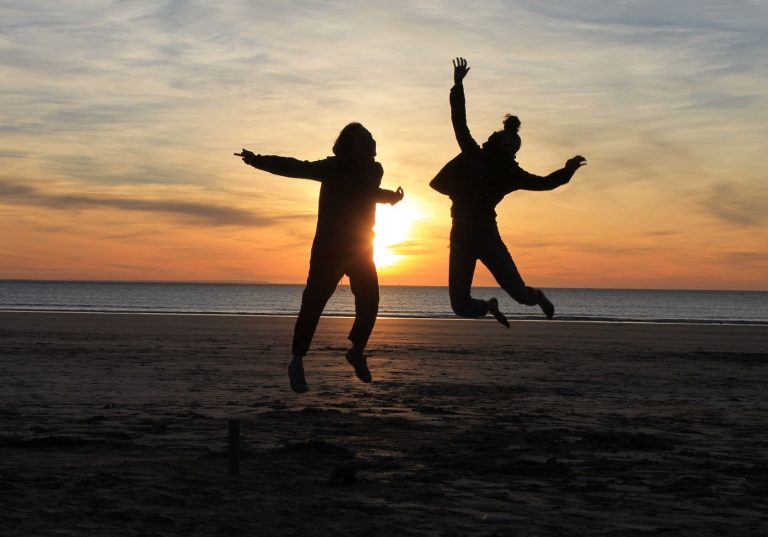 Eine andere Perspektive hilft Dir! Zwei Personen springen fröhlich am Strand bei Sonnenuntergang.