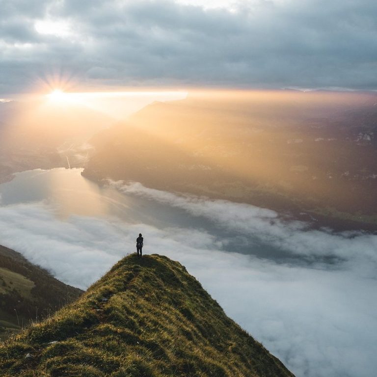 Eine andere Perspektive hilft Person steht auf einem Berghang mit Blick auf einen Fluss und Sonnenstrahlen durch Wolken.