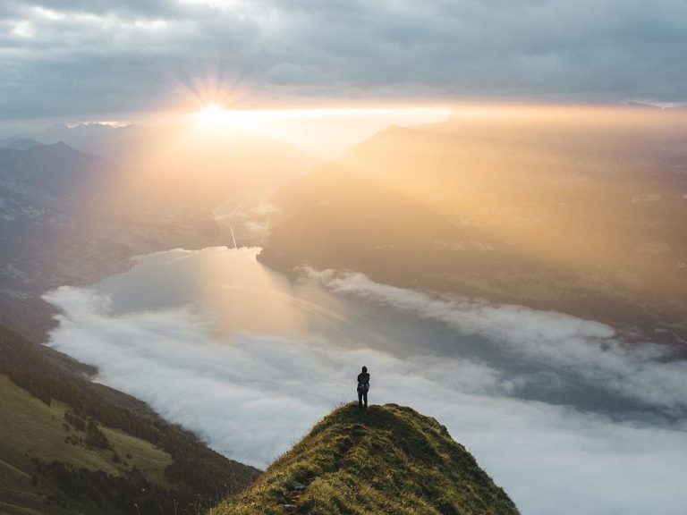 Eine andere Perspektive hilft! Eine Person steht auf einem Hügel, während die Sonne über neblige Landschaft aufgeht.