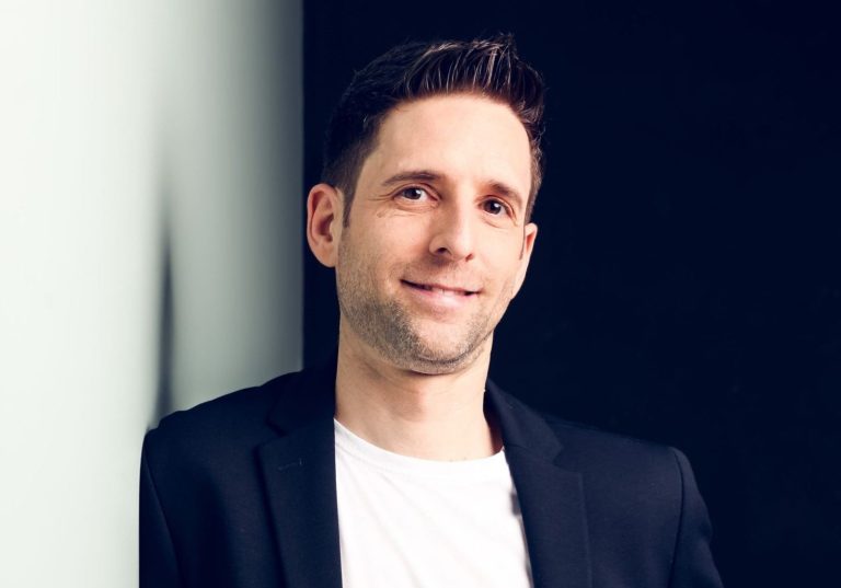 Psychologischer Berater, Coach, Mentor Mann in lässiger Kleidung, lächelnd vor dunklem Hintergrund, steht an einer Wand.